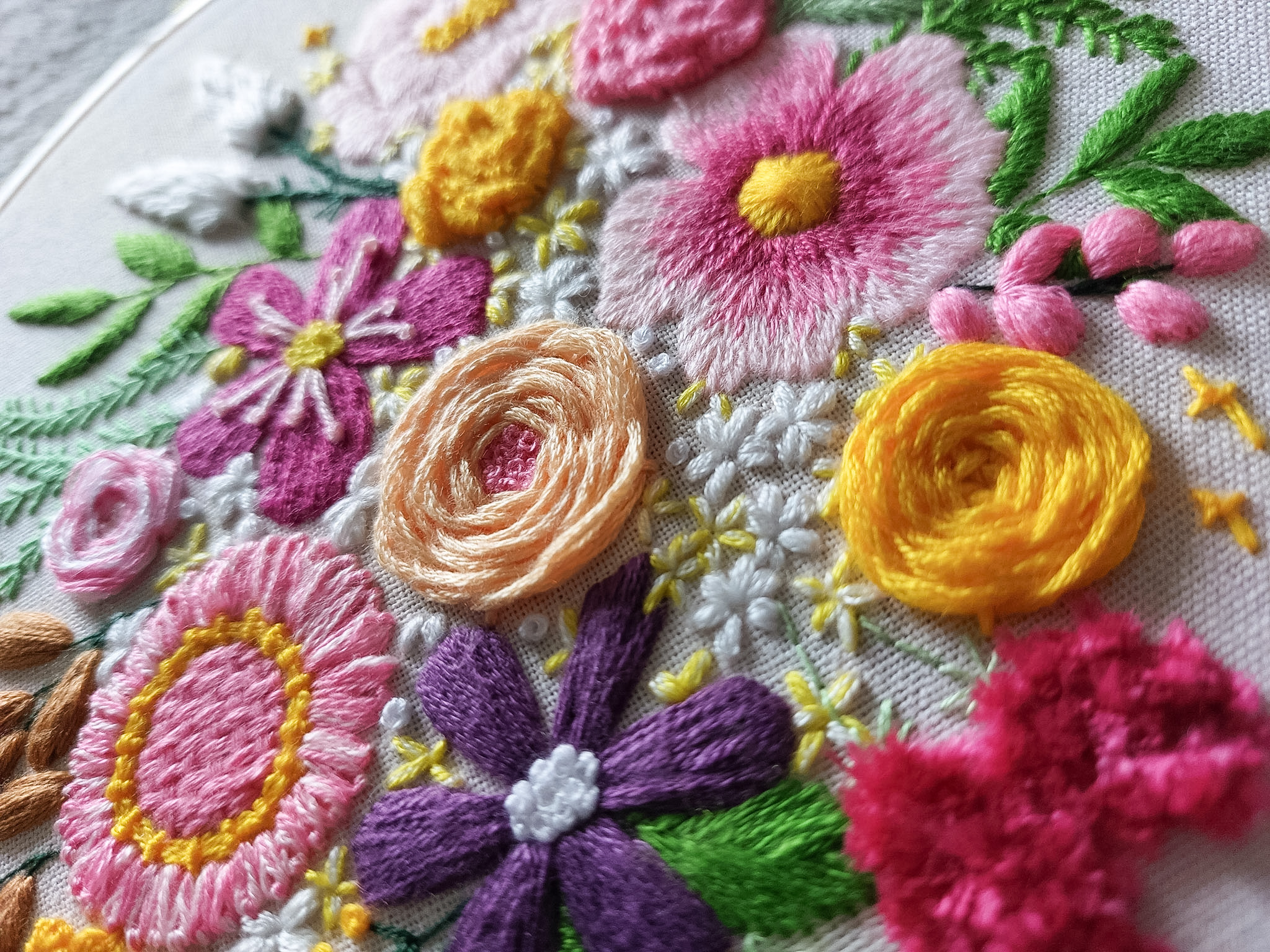 A close up of bright and beautiful floral embroidery stitches, showcasing a mix of advanced embroidery stitches and neat satin stitch. This is the 'Blooming Florals' pattern from embroidery membership Bloom Embroidery Academy.