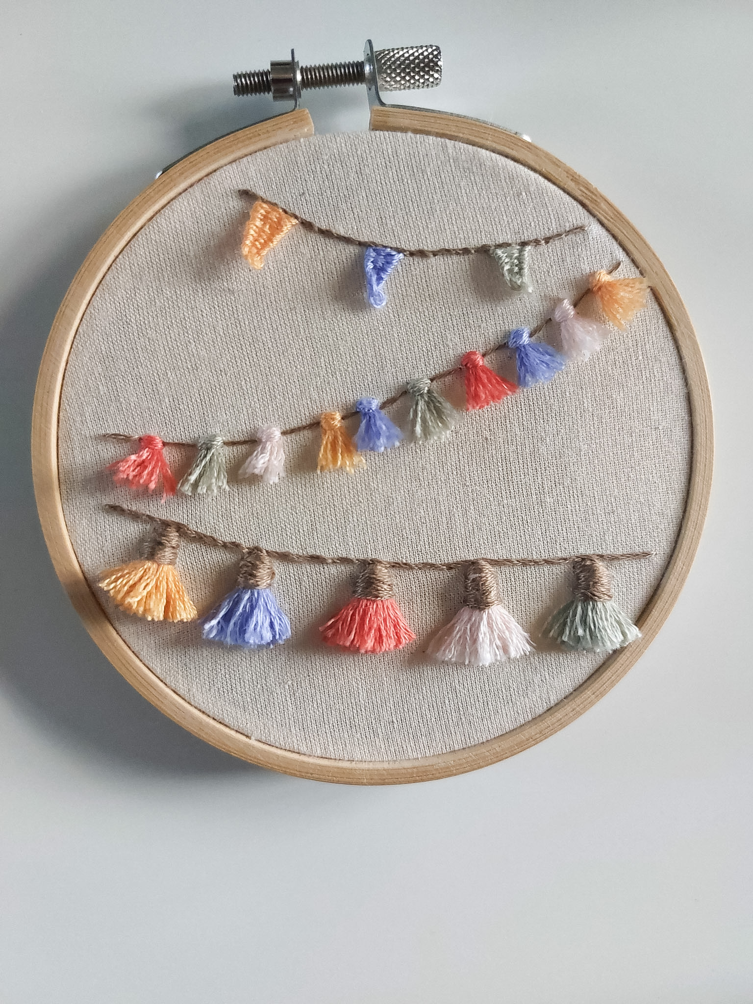 An embroidery hoop filled with pastel bunting, using advanced embroidery stitches learned through the embroidery membership, Bloom Embroidery Academy