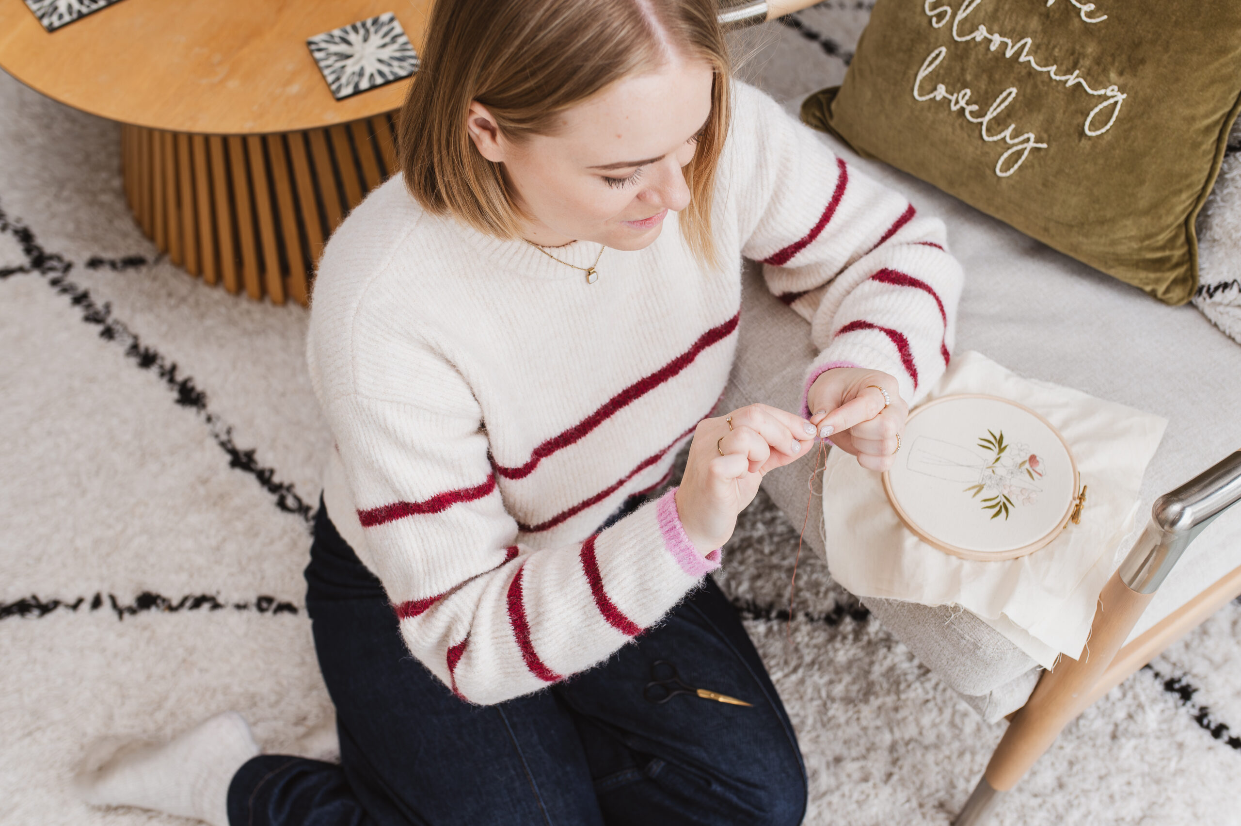 Sophie sat on a rug in cosy clothing, preparing thread to start stitching.
