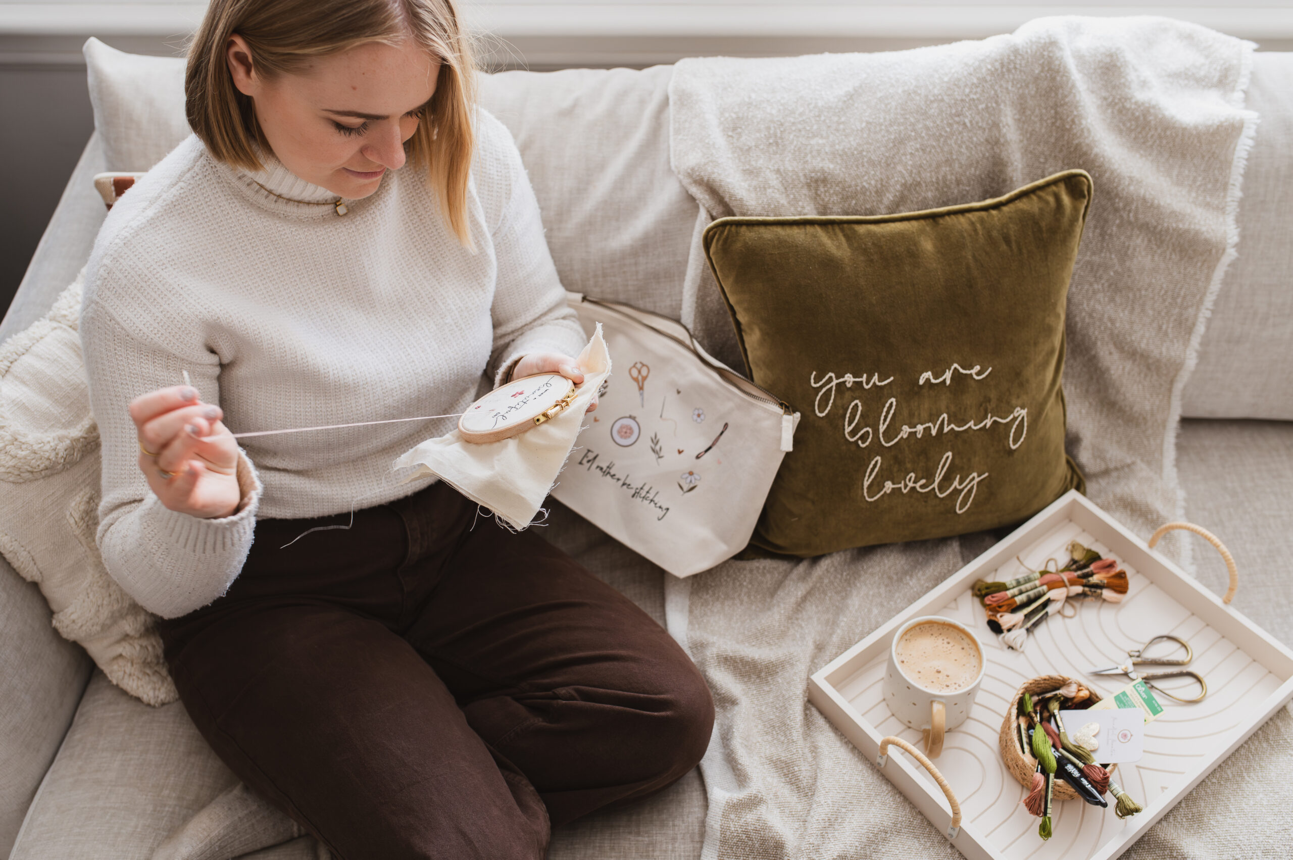 Sophie sat on a cosy sofa stitching her latest embroidery project, holding her hoop in her hand