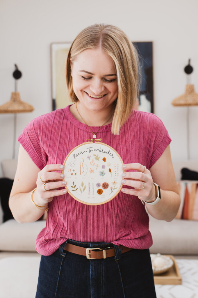 Sophie holding up an embroidery hoop with a sampler embroidery pattern that says 'learn to embroider', from the Introduction to Embroidery online beginner course
